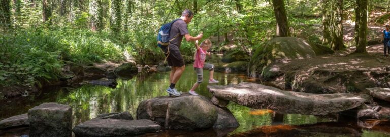 Un père et sa fille se promènent sur les rochers qui parsèment la rivière d’Argent au cœur de la forêt d’Huelgoat.