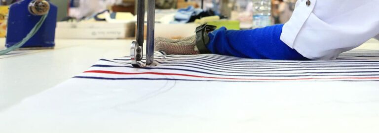 Gros plan sur une machine à coudre et tissu dans l’atelier Armor Lux.