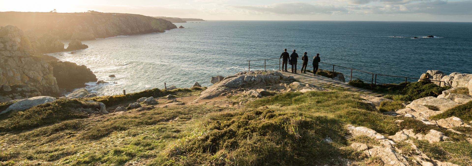 Quatre personnes admirant la vue depuis un belvédère surplombant l’océan Atlantique à la Pointe du Raz, dans le Finistère, au cœur d’un paysage côtier sauvage et majestueux.