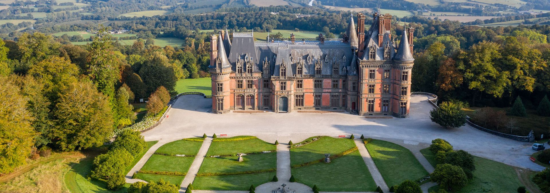 Vue aérienne du château de Trévarez et de ses jardins à la française, entourés de forêt.