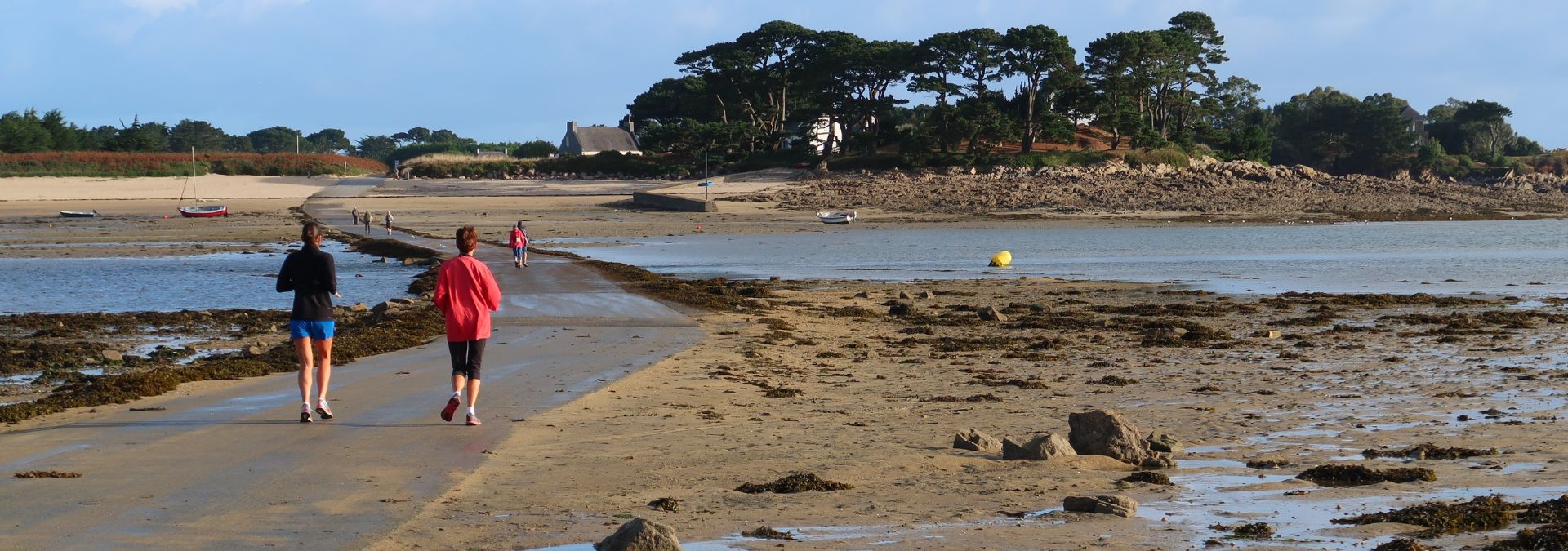 Promeneurs sur le passage submersible menant à l’île Callot à marée basse, avec vue sur l’île et le littoral du Finistère.