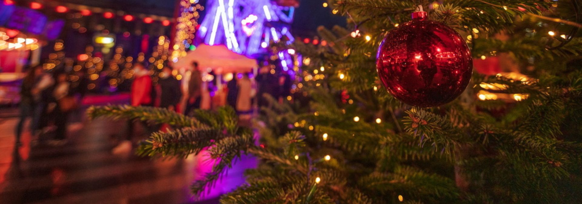 Boule de Noël rouge sur un sapin avec lumières et grande roue floutée en arrière-plan.